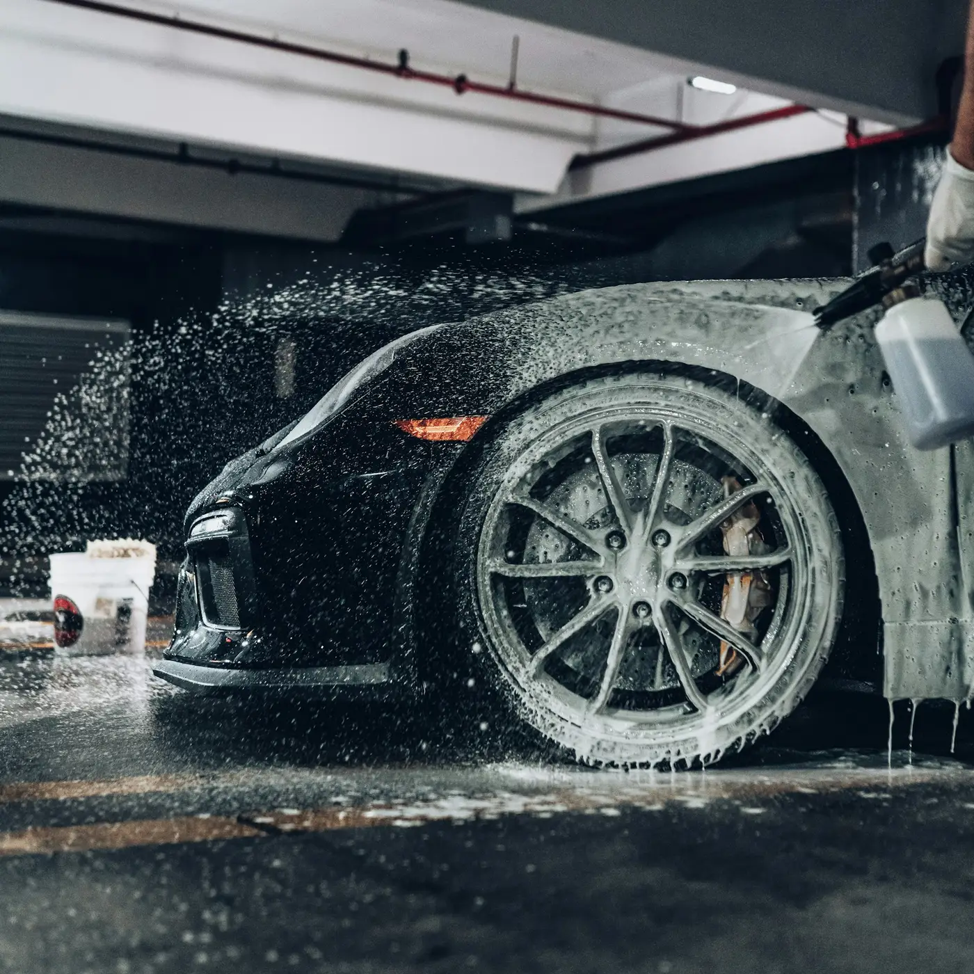 A detailer spraying soap foam onto a black sports car