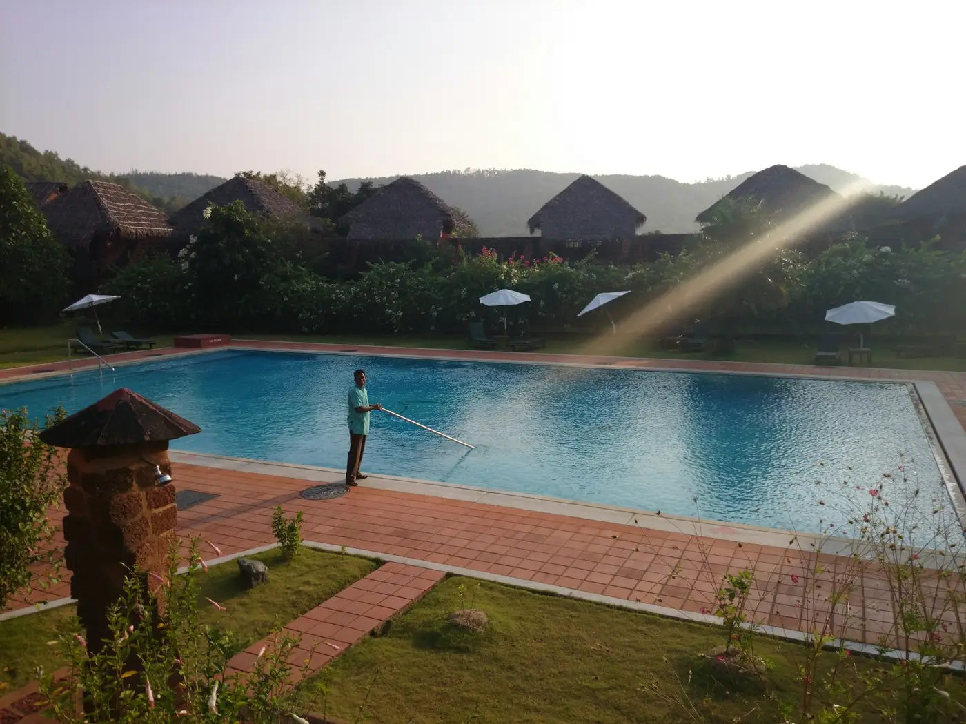 A pool technician cleaning a backyard pool on a sunny morning